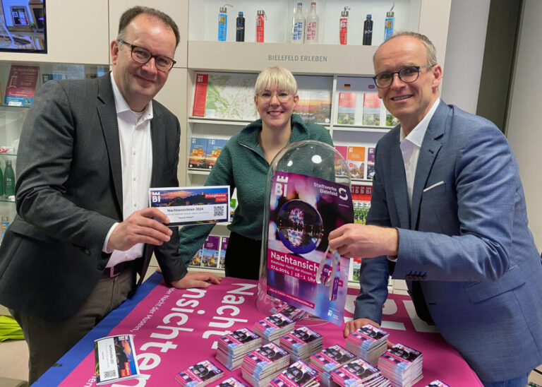 (v.l.) Martin Knabenreich und Katharina Schilberg (Bielefeld Marketing) stellen gemeinsam mit Martin Uekmann (Stadtwerke Bielefeld) das Programm für die Nachtansichten 2024 in der Tourist-Information vor. Foto: Bielefeld Marketing GmbH