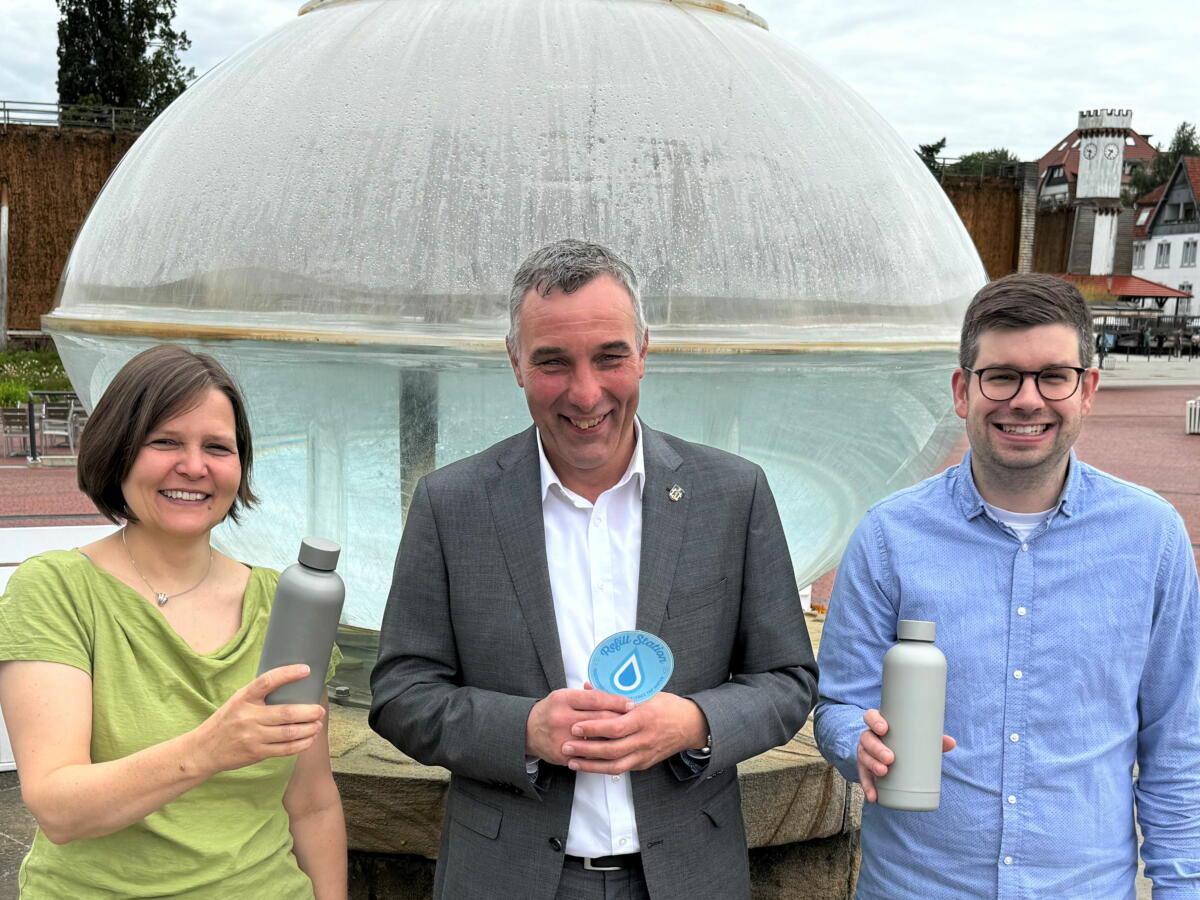 Die Stadt Bad Salzuflen füllt auf: An einem der ersten Standorte in der Kurstadt, am Kurgastzentrum, wird ein Refill-Aufkleber aufgebracht. Neben den städtischen Einrichtungen rufen (v.l.) Klimaschutzbeauftragte Susanne Lübker, Bürgermeister Dirk Tolkemitt und Jan Feldmeier die hiesigen Geschäfte und Lokale zum Mitmachen auf, damit Bürger*innen und Gäste sich kostenfreies Leitungswasser in selbst mitgebrachten Trinkflaschen abfüllen lassen können. Foto: © Stadt Bad Salzuflen