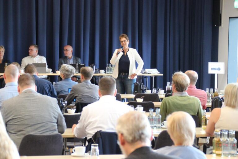 Sabine Beine begrüßt die neugierigen Zuhörer zur Auftaktveranstaltung zum Aufbau einer Trinkwassernotversorgung in der Phoenix-Contact-Arena. Auf dem Podium hinter ihr sind (v.r.) mit Michael Eich und Florian Scholle sowie Dr. Ina Wienand ein Teil der Referentinnen und Referenten zu sehen. Foto: Kreis Lippe