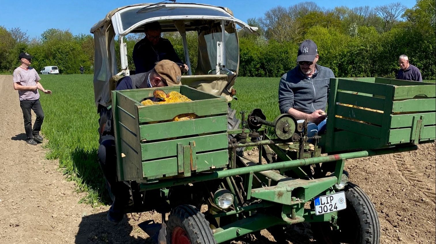 Drei Männer an einem grünen Oldtimer-Trecker mit Holzkisten auf einem sonnigen Feld