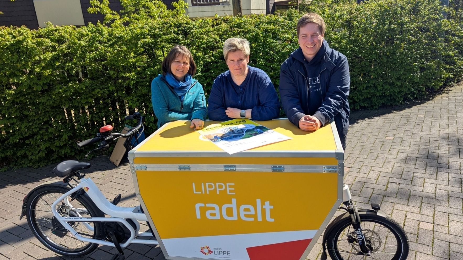 Drei lächelnde Personen stehen hinter einem gelben Lastenfahrrad mit „LIPPE radelt“ Aufschrift und einem
