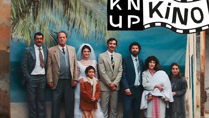 Eine Familie, darunter ein Brautpaar und ein Kind, posiert vor einer tropischen Kulisse