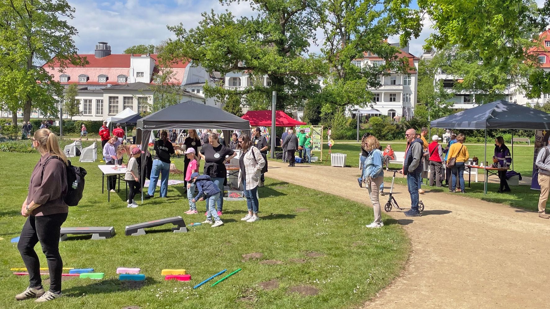 Zahlreiche Besucher versammeln sich an Vereinsständen in einem sonnigen Kurpark mit Bäumen, Grasflächen und