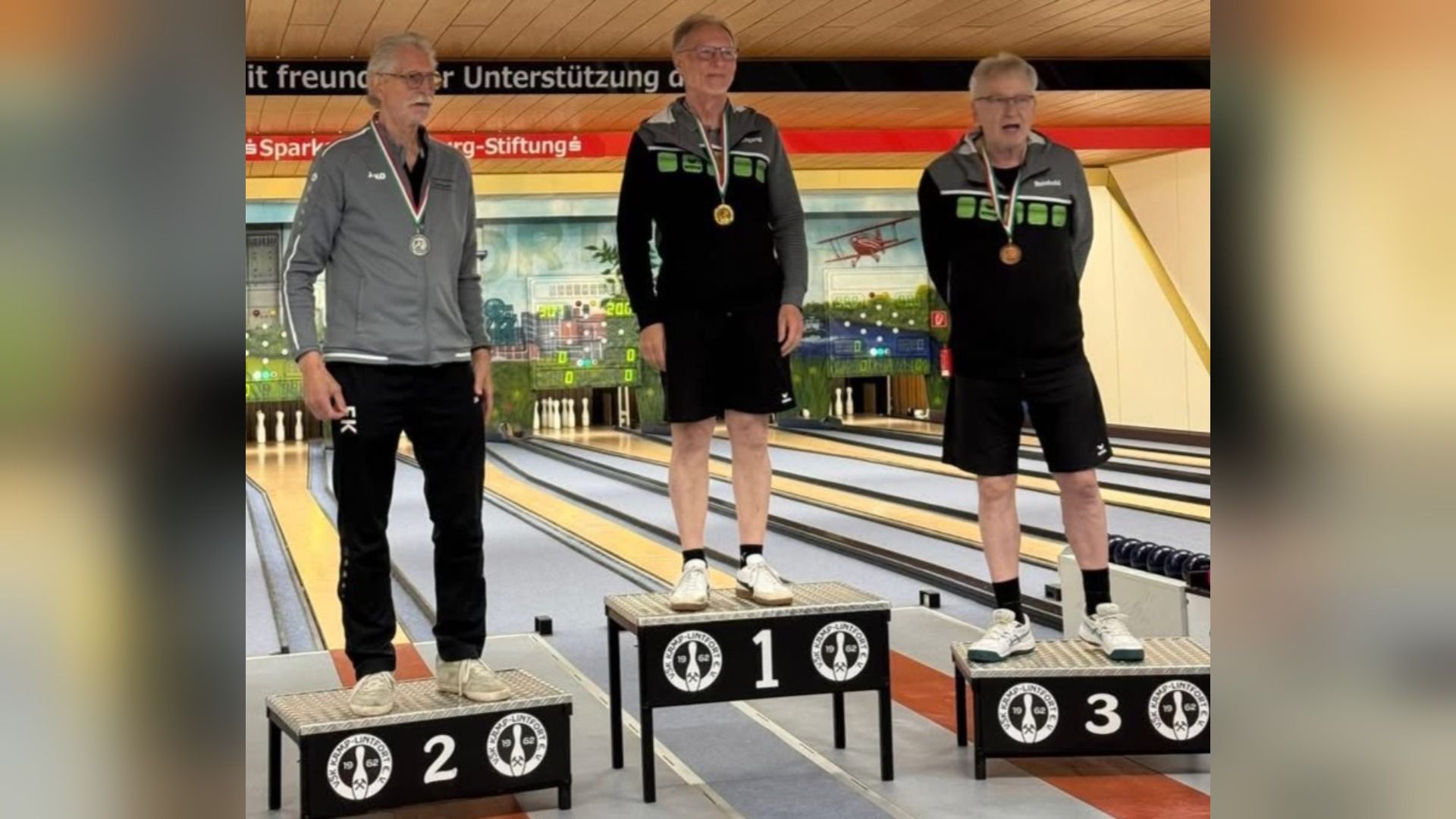 Drei Männer in Sportkleidung mit Medaillen auf dem Siegertreppchen in Kamp-Lintfort