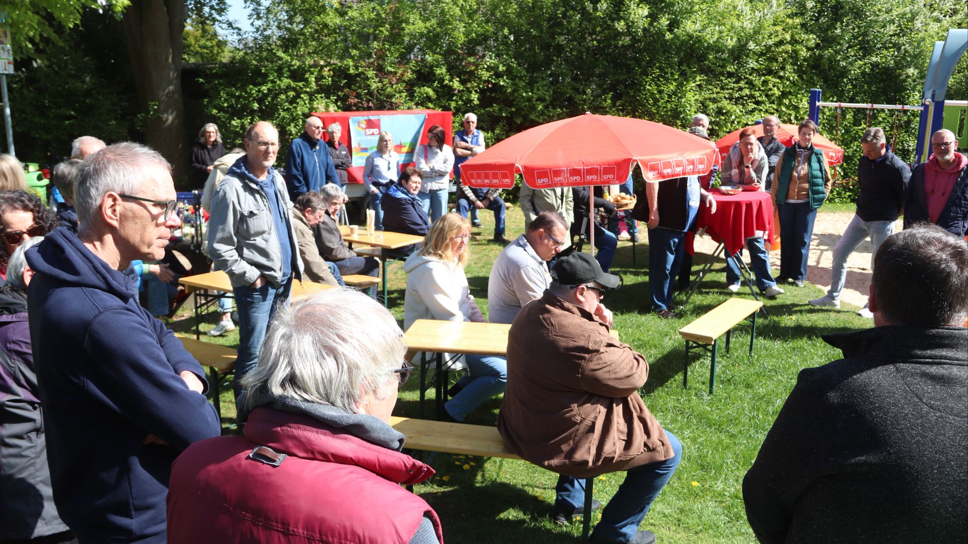 Viele Menschen auf einer SPD-Veranstaltung im Freien in Oerlinghausen, umgeben von roten Sonnenschirmen und Bänken