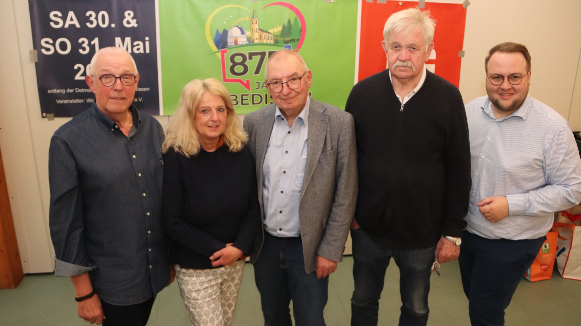 Fünf Personen, vier Männer und eine Frau, stehen vor einem Banner mit der Aufschrift 875 Jahre Ubbedissen