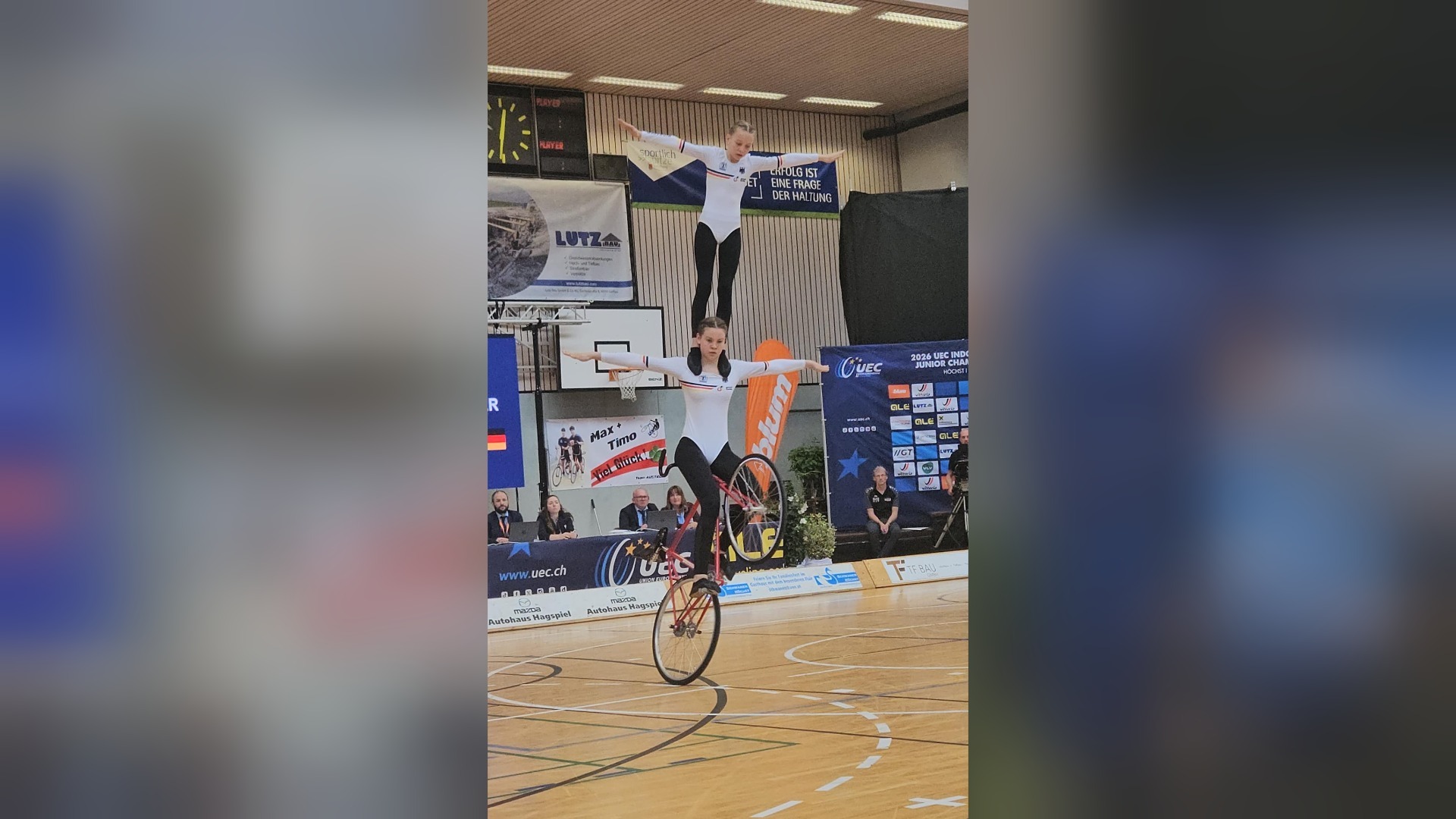 Marlene und Greta Engelkemeier in weißen Sportanzügen, eine balanciert auf einem Einrad, die andere auf ihren Schultern