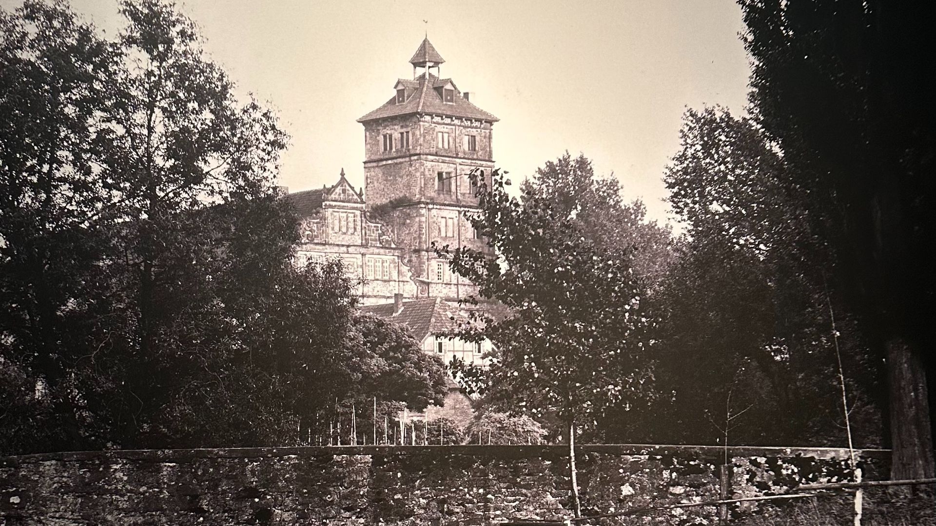 Schloss Brake, ein großes Schlossgebäude mit zentralem Turm, umgeben von dichtem Grün und einer Steinmauer im