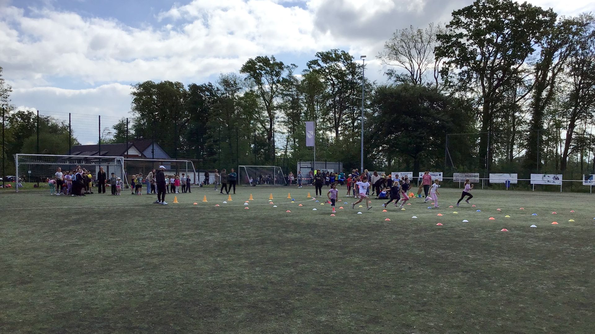 Kinder und Erwachsene auf einem Sportplatz mit vielen farbigen Hütchen, einige Kinder rennen über den Platz