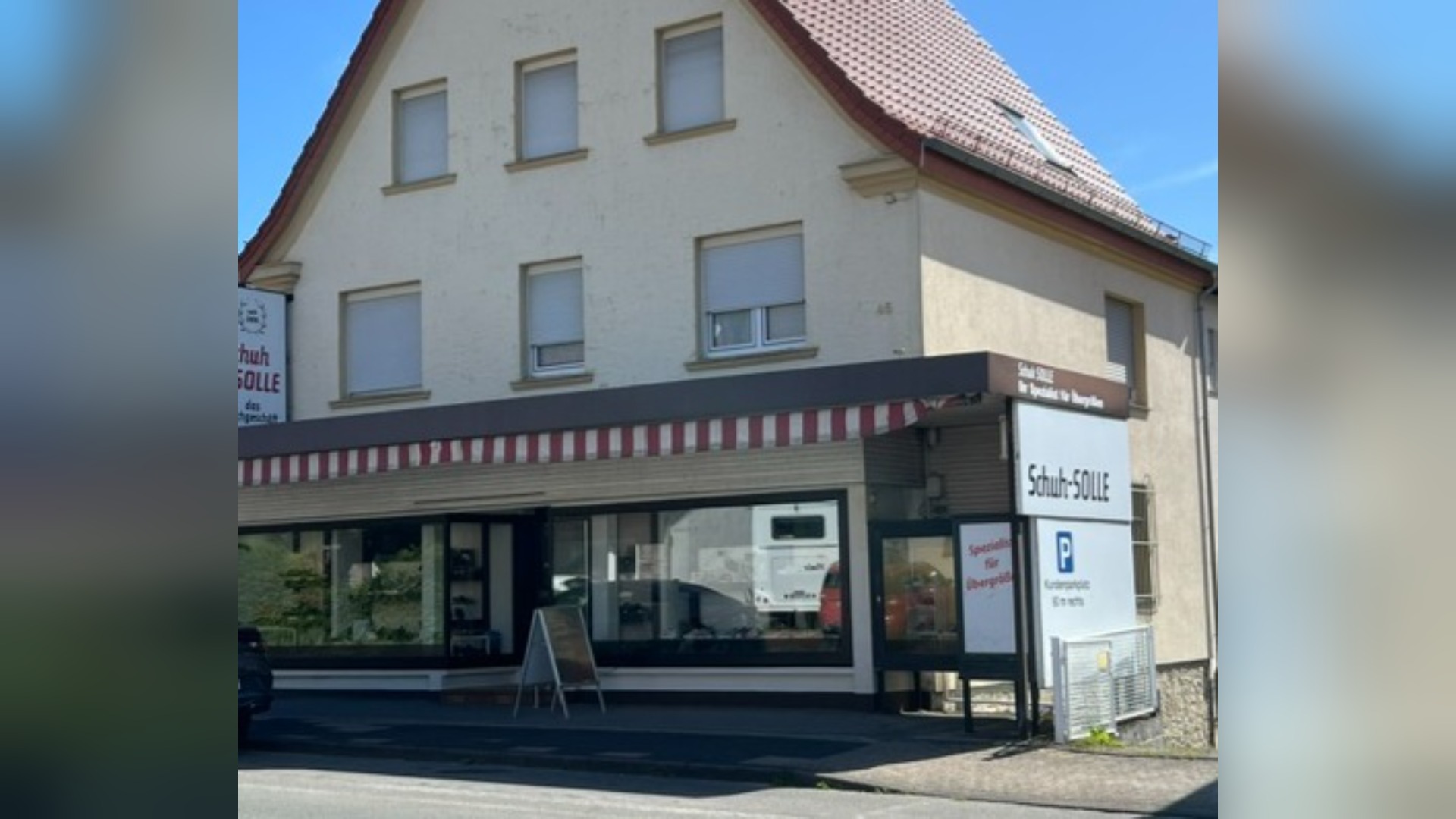 Schuhgeschäft Schuh-SOLLE: ein mehrgeschossiges Gebäude mit Schaufenstern, gestreiftem Vordach und Parkplatzschild an