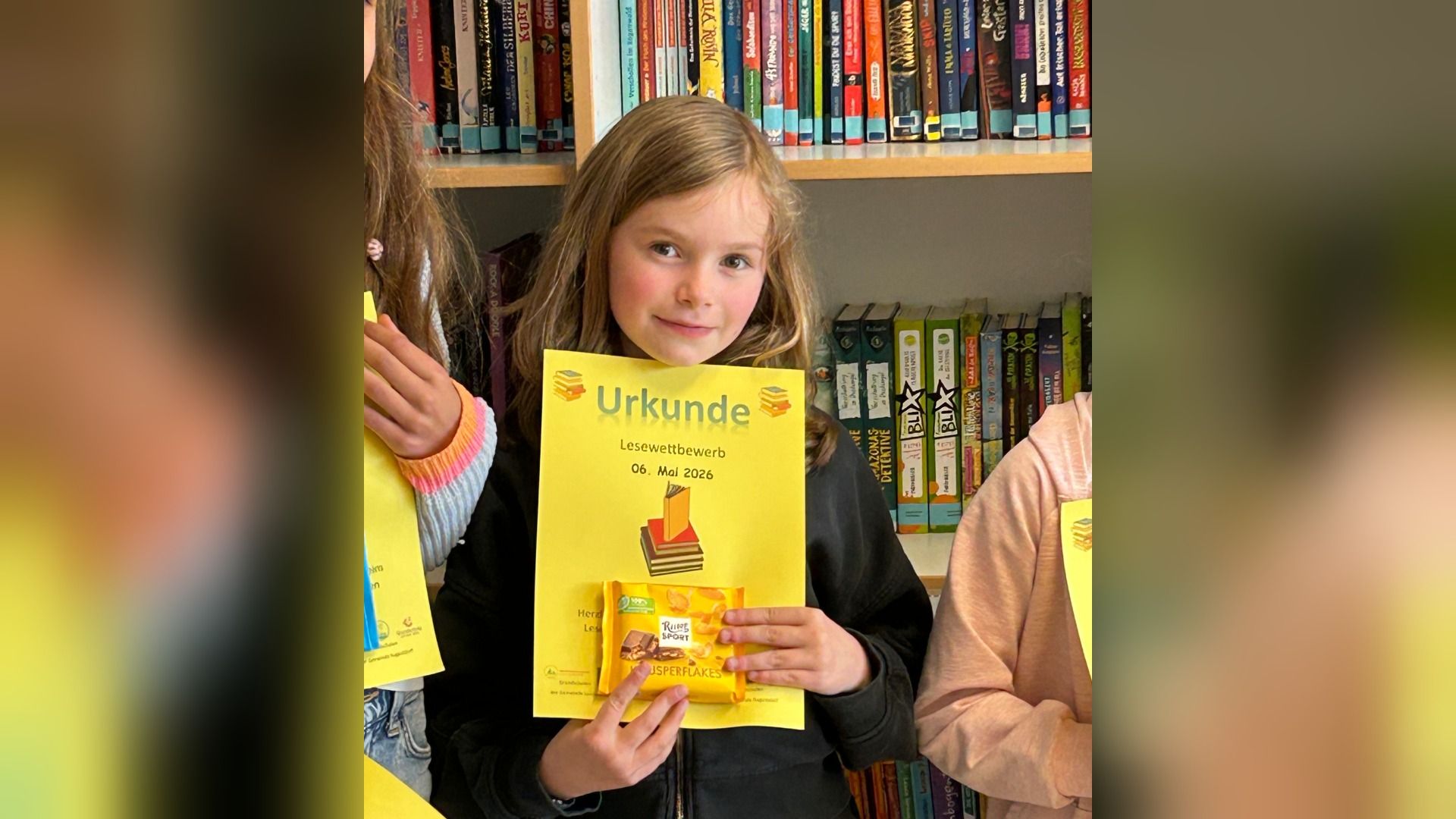 Amilia Simpson lächelt und hält eine gelbe Urkunde vom Lesewettbewerb und eine Packung Knusperflakes vor einem