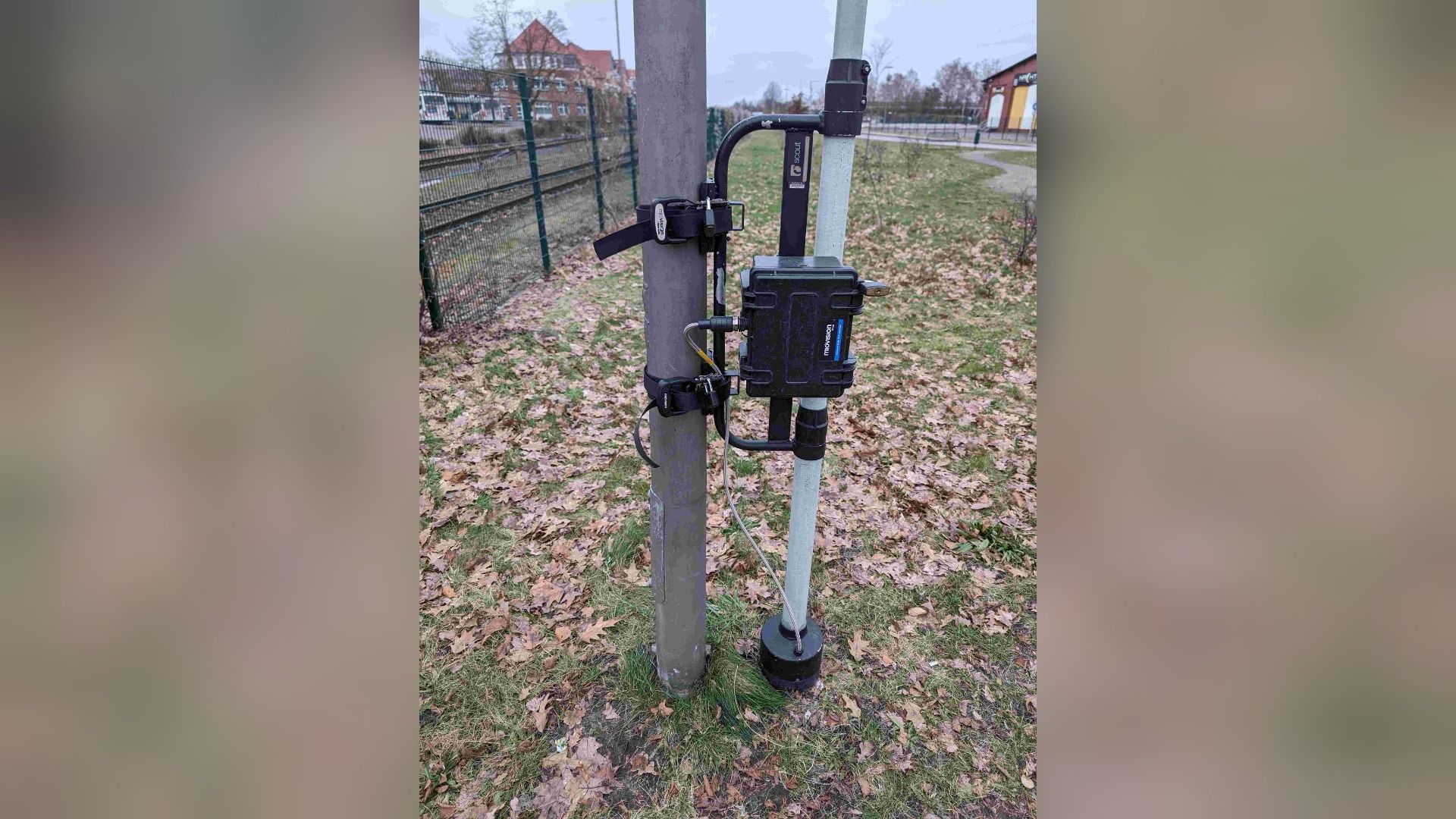 Kamerasystem 'movision scout' an zwei Pfählen auf Gras mit Herbstlaub vor einem Zaun und Gebäuden