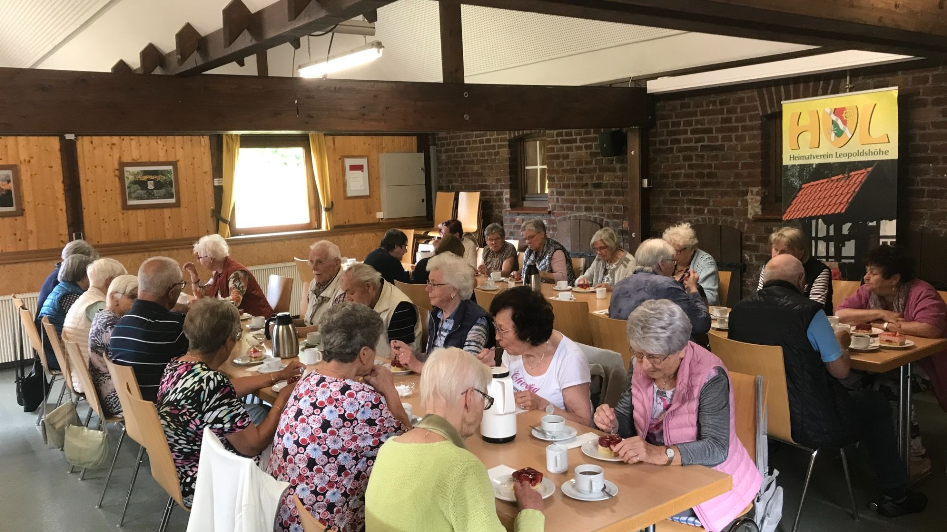 Senioren und Seniorinnen des Heimatvereins Leopoldshöhe sitzen an Tischen bei Kaffee und Kuchen und unterhalten sich