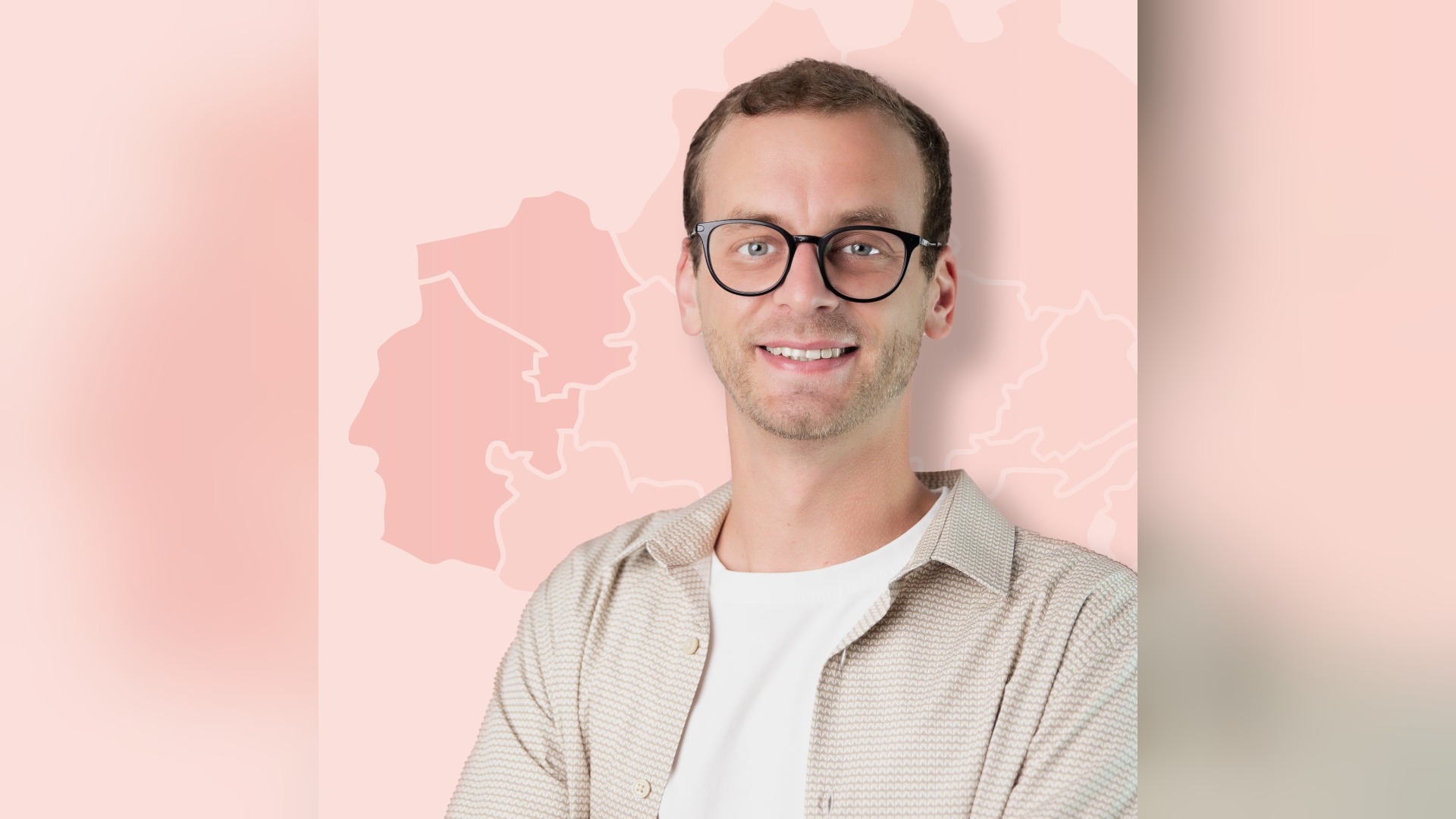 Ein lächelnder junger Mann mit Brille und beigem Hemd vor einem hellrosa Hintergrund mit dezenten Umrissen