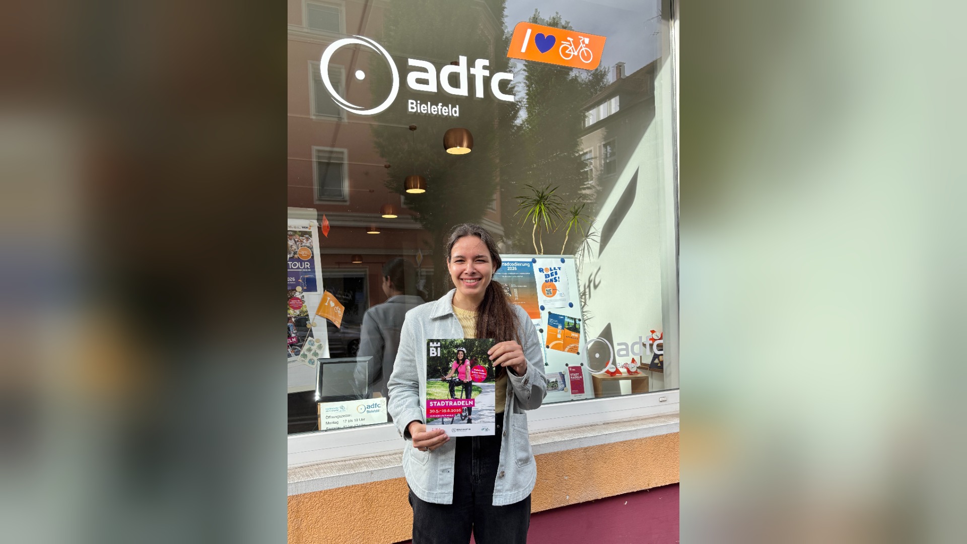 Lächelnde junge Frau hält einen Flyer für das STADTRADELN 2026 vor dem ADFC-Laden in Bielefeld