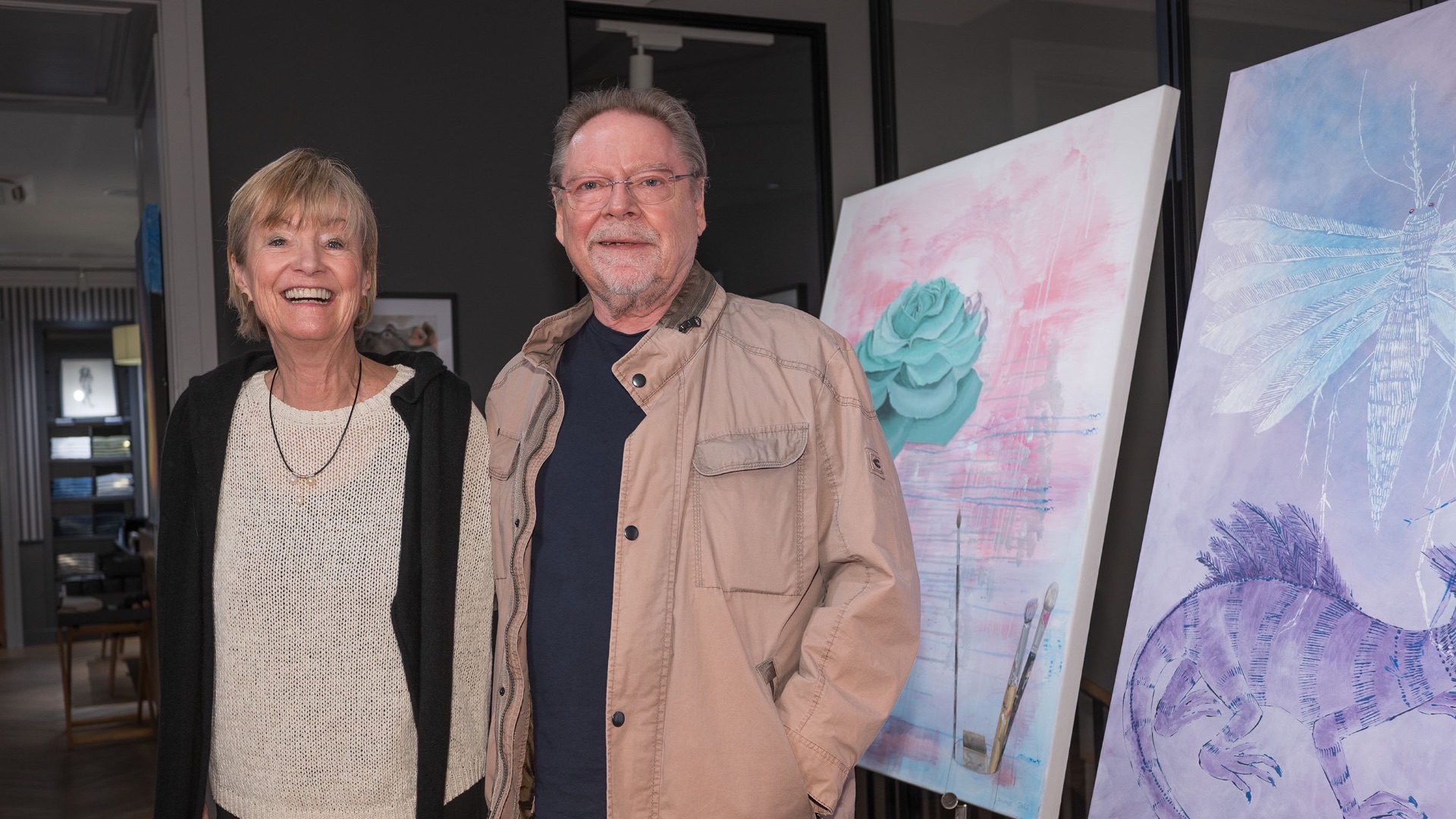 Jürgen von der Lippe und Anne Dohrenkamp lächeln neben zwei Gemälden mit Blumen und Tieren in einem Raum