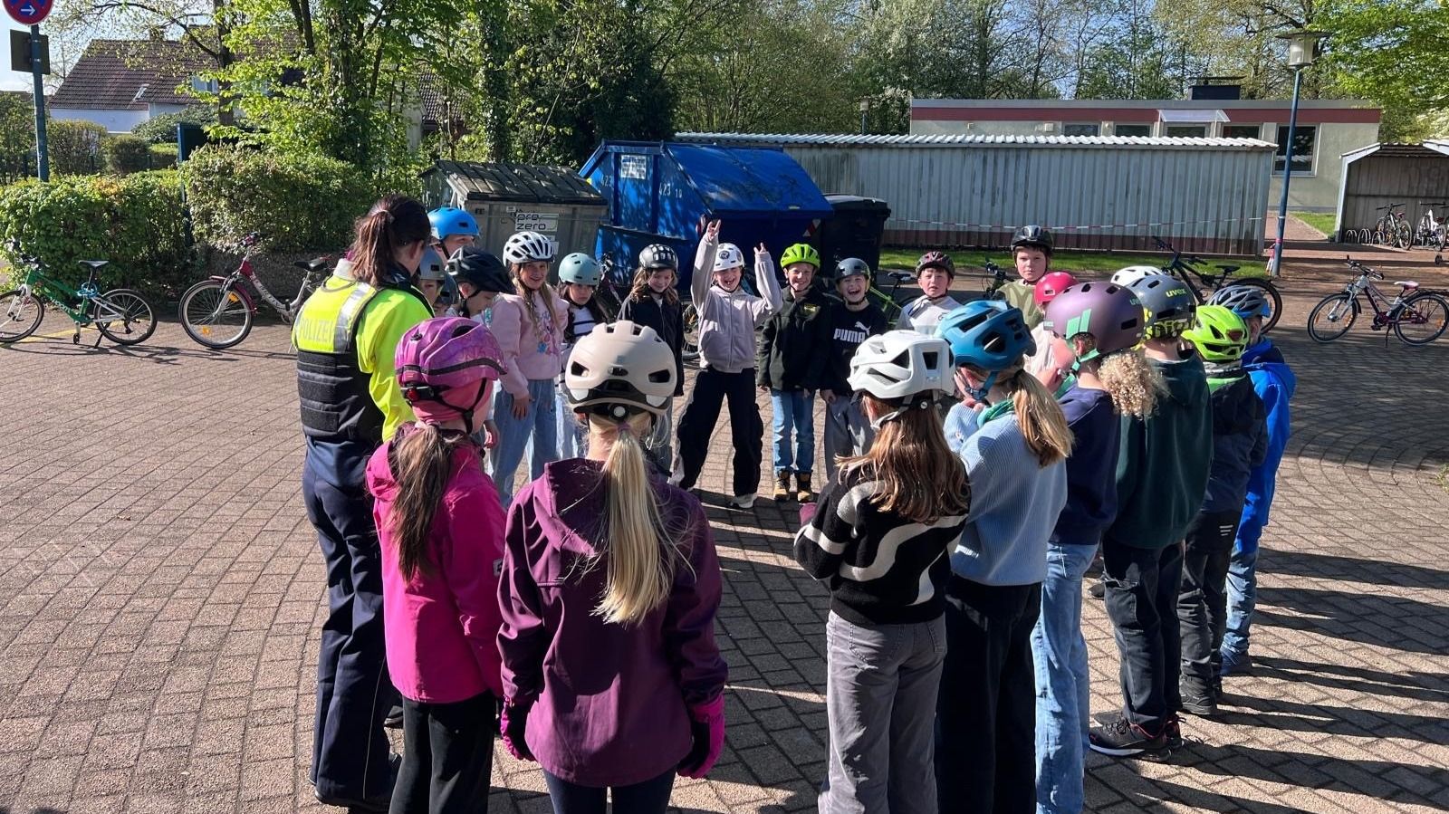 Viertklässler der Grundschule Nord mit bunten Helmen und eine Polizistin stehen auf dem Schulhof, ein Kind jubelt
