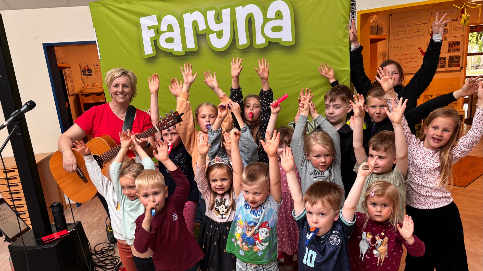 Faryna spielt Gitarre und lächelt, während viele Kinder mit erhobenen Händen und Partytröten ausgelassen jubeln