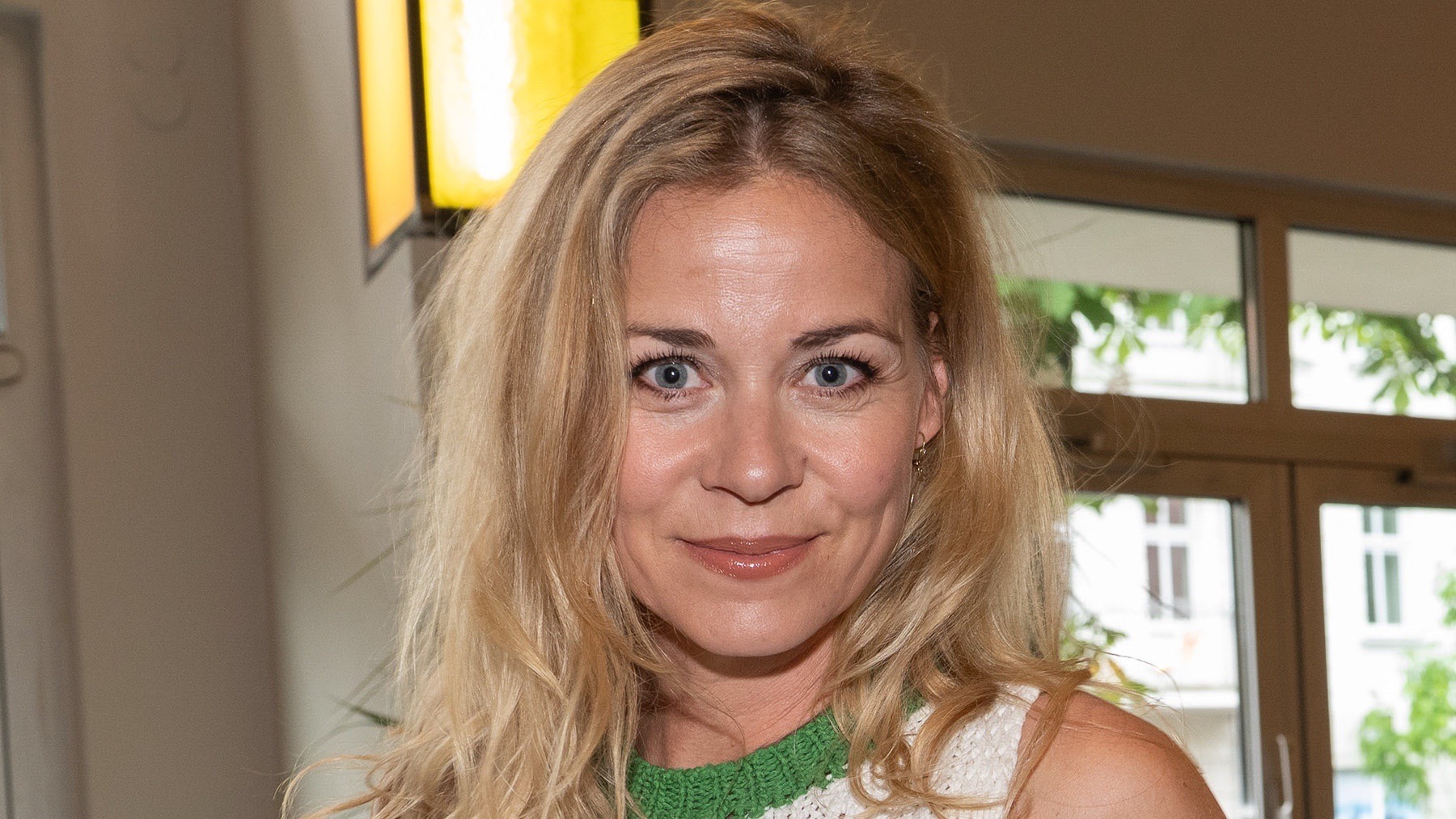 Nahaufnahme von Jessica Ginkel mit blonden Locken, blauen Augen und einem leichten Lächeln vor unscharfem Hintergrund
