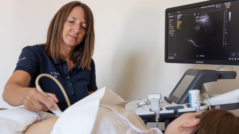 Physician Assistant Silke Teufel führt bei einer liegenden Person eine Ultraschalluntersuchung des Bauches durch