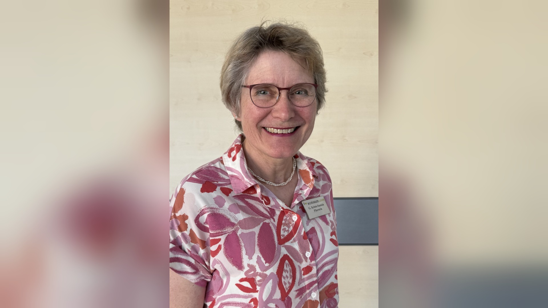 Lachende Frau mit Brille und gemustertem Oberteil, ihr Namensschild zeigt G. Krist-Suselo Pfarrerin