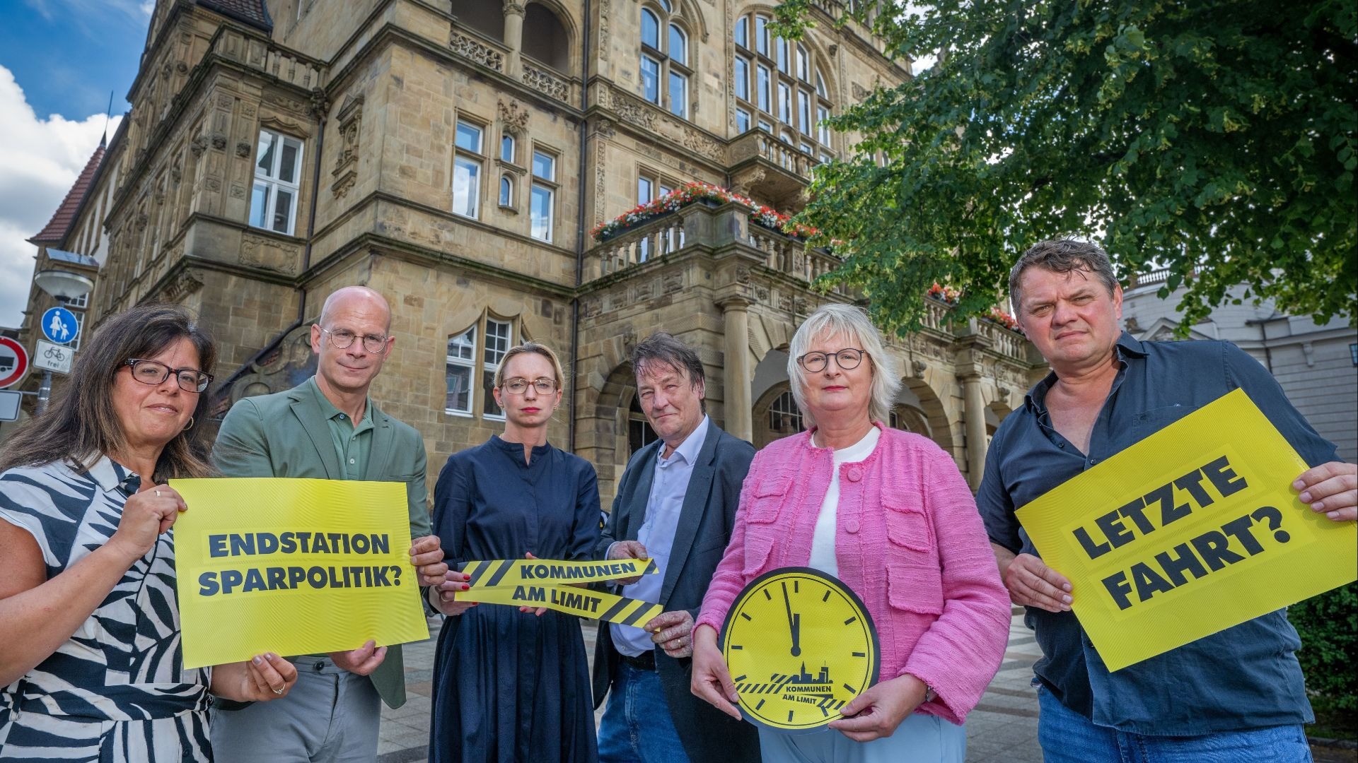 Sechs Personen protestieren mit gelben Schildern „Endstation Sparpolitik“, „Kommunen am Limit“ und „Letzte Fahrt?“ vor