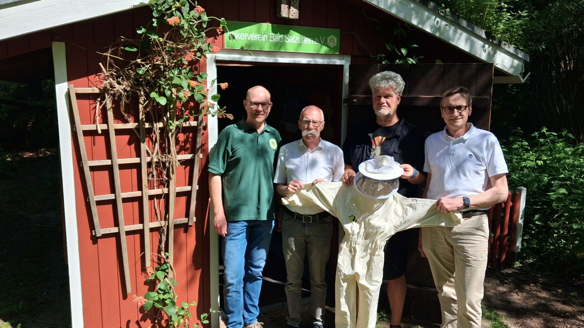Vier Männer präsentieren einen Imkeranzug vor dem roten Bienenhaus des Imkervereins Bad Salzuflen
