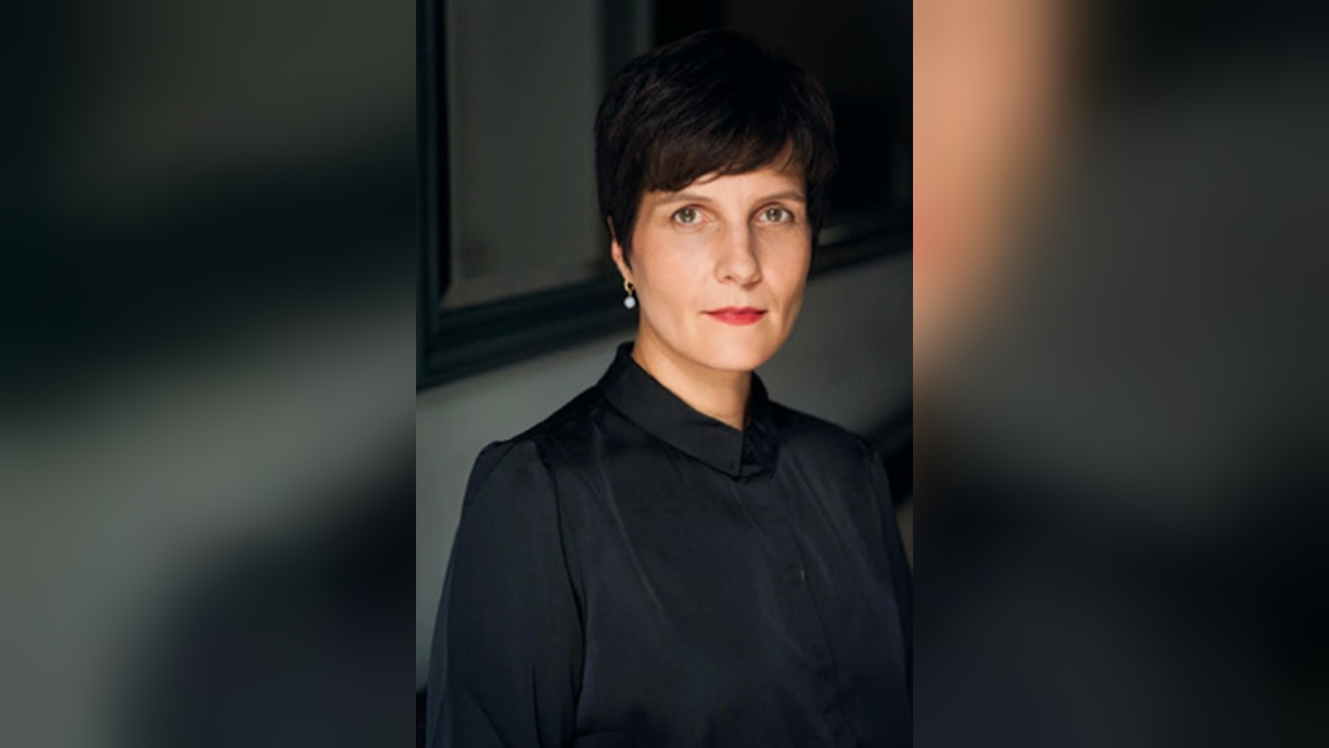 Anne Stern, eine Frau mit kurzen dunklen Haaren, schwarzer Bluse und Perlenohrring, blickt in die Kamera