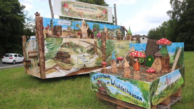 Zwei große Holzdarstellungen einer Wichtel-Miniaturwelt mit Pilzen, Wichtel-Figuren und Umweltschutzbotschaften am