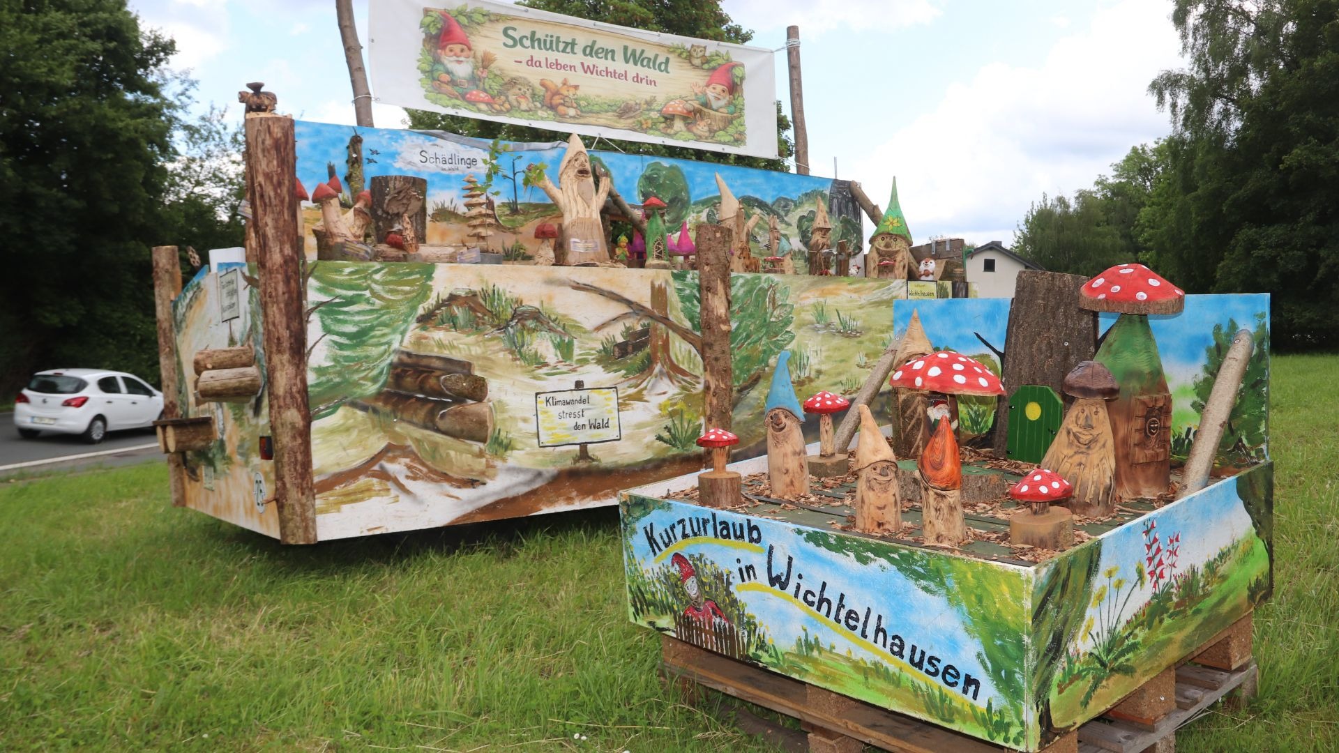 Zwei große Holzdarstellungen einer Wichtel-Miniaturwelt mit Pilzen, Wichtel-Figuren und Umweltschutzbotschaften am