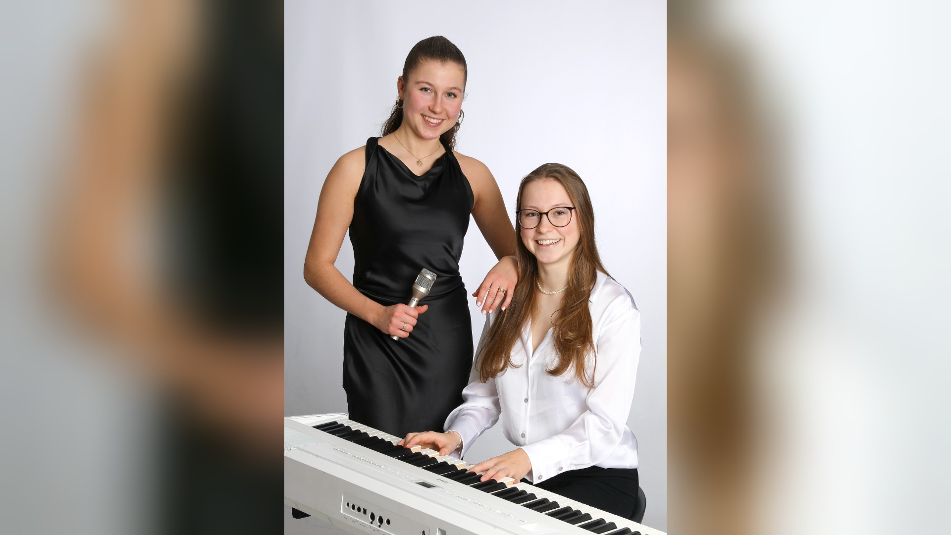 Lina und Julie Holwitt lächeln, Lina mit Mikrofon stehend, Julie am weißen Keyboard spielend