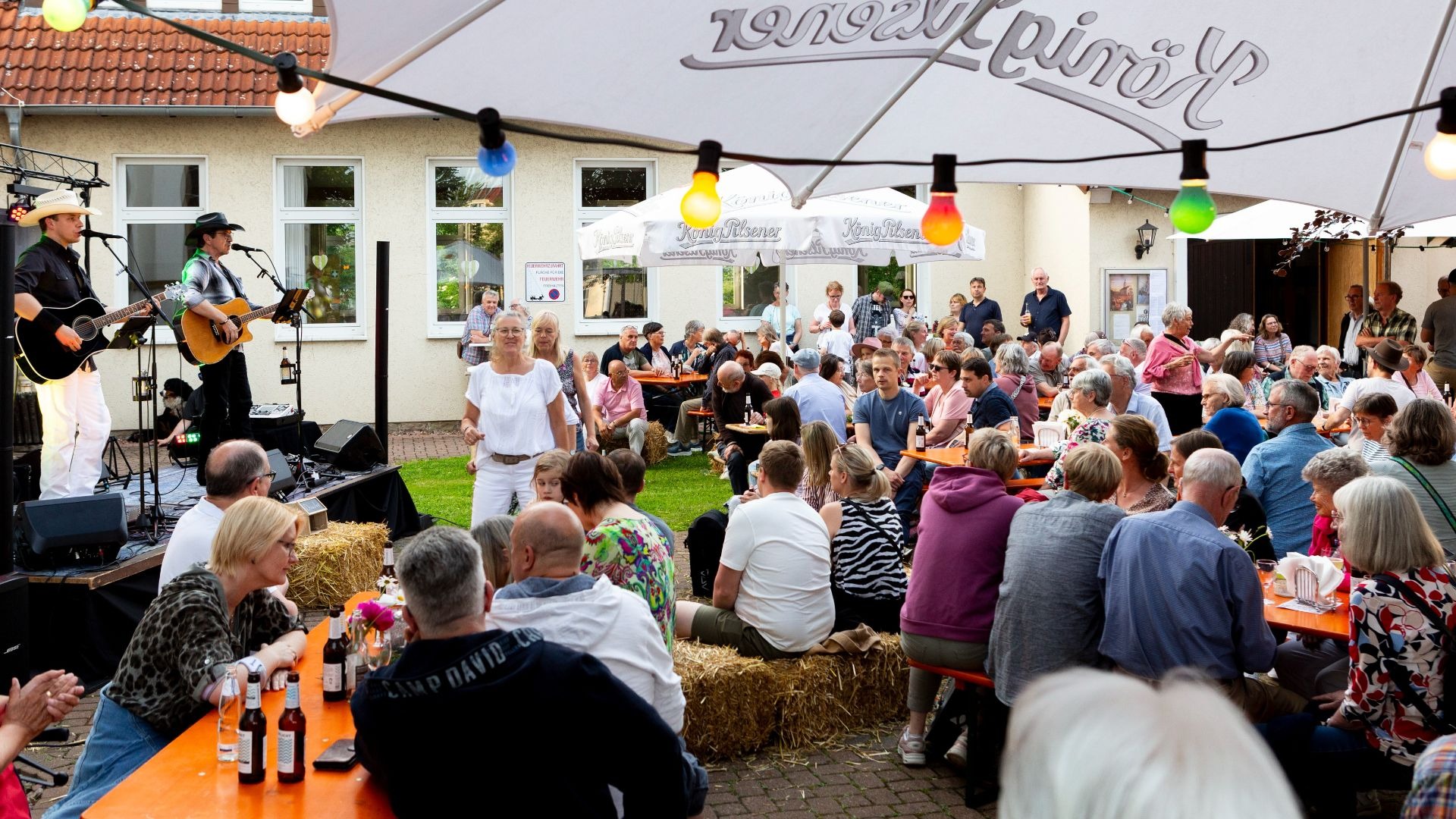 Zwei Musiker mit Gitarren und Cowboyhüten spielen auf einer Bühne vor einem großen Publikum an einem Sommerabend
