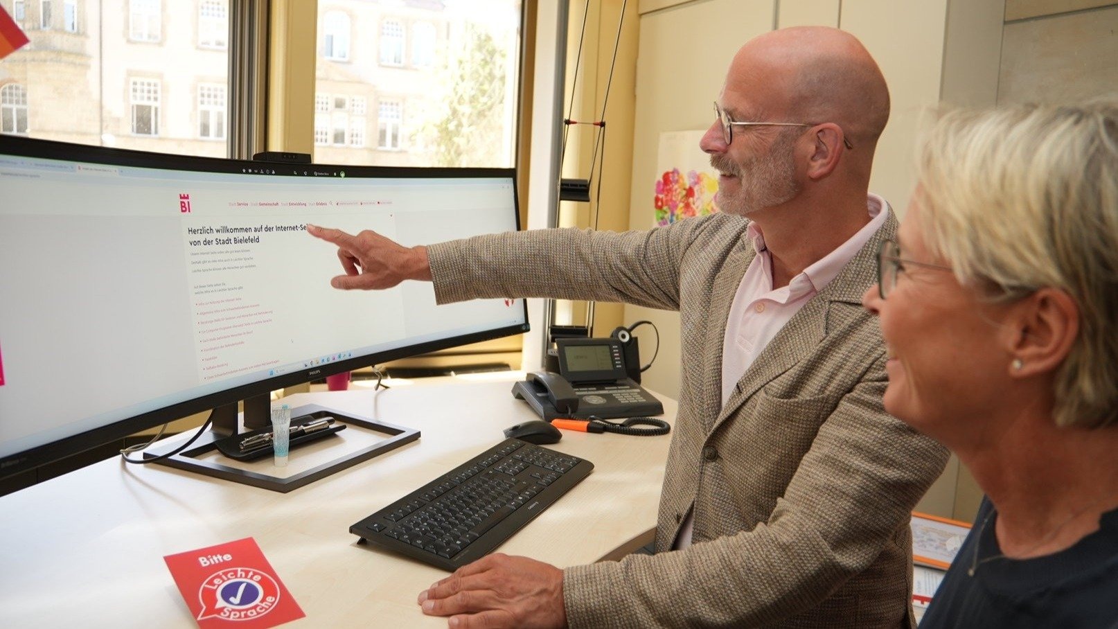 Mann zeigt Frau am Computerbildschirm die Website der Stadt Bielefeld mit Informationen zu Leichter Sprache