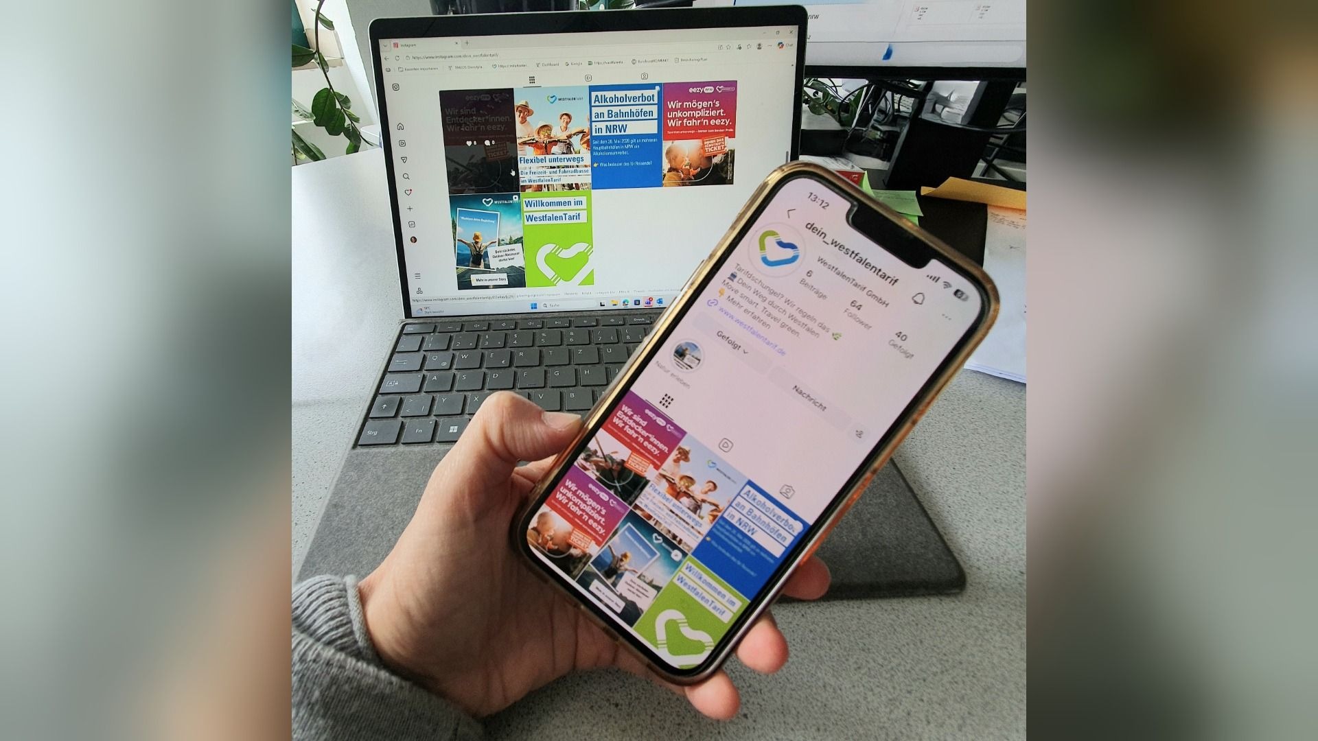 Eine Hand hält ein Smartphone mit dem Instagram-Profil von @dein_westfalentarif vor einem Laptop, der dasselbe zeigt