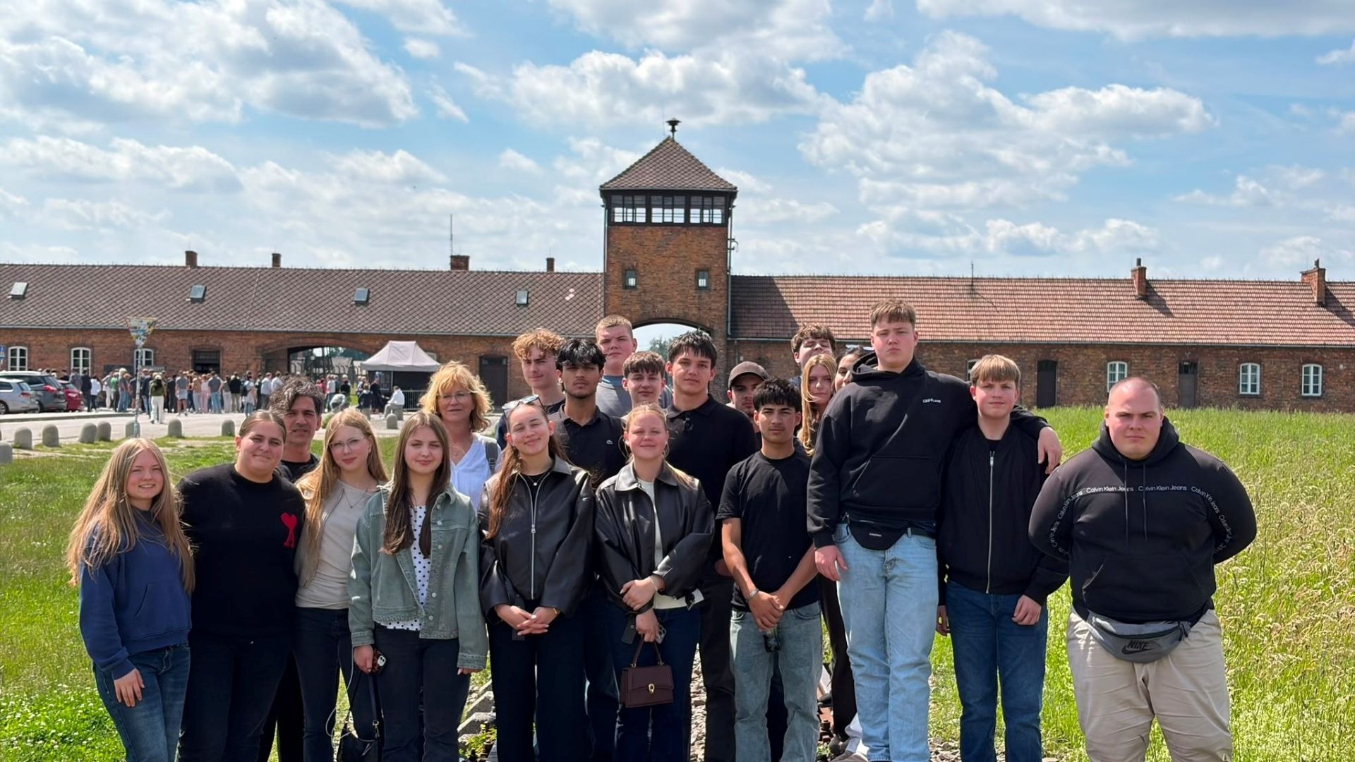 Gruppe junger Menschen und Erwachsene vor dem Backsteintorhaus des ehemaligen Konzentrationslagers Auschwitz-Birkenau