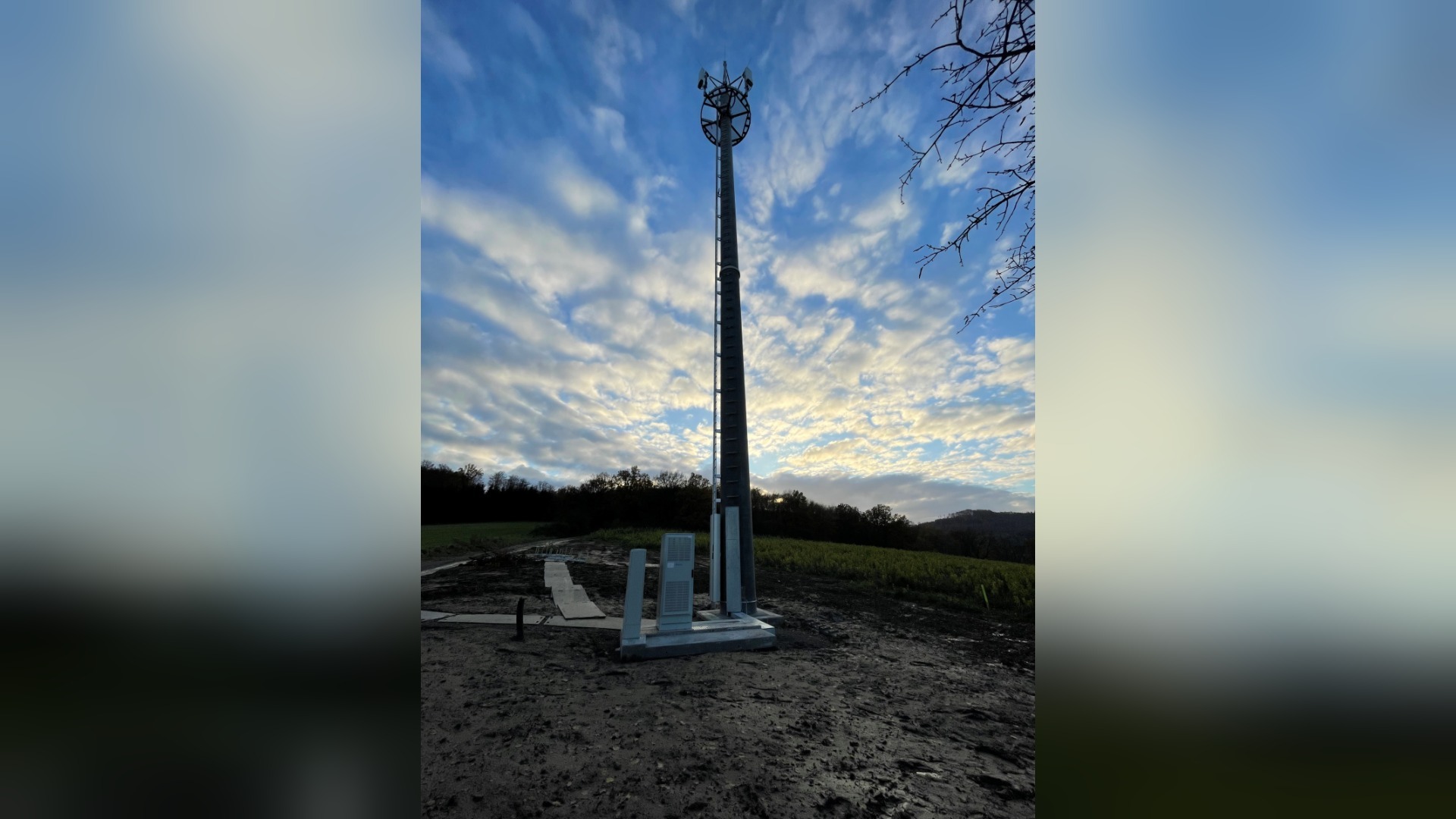 Hoher Mobilfunkmast mit Antennen auf einer Anhöhe unter bewölktem Himmel und Wäldern im Hintergrund
