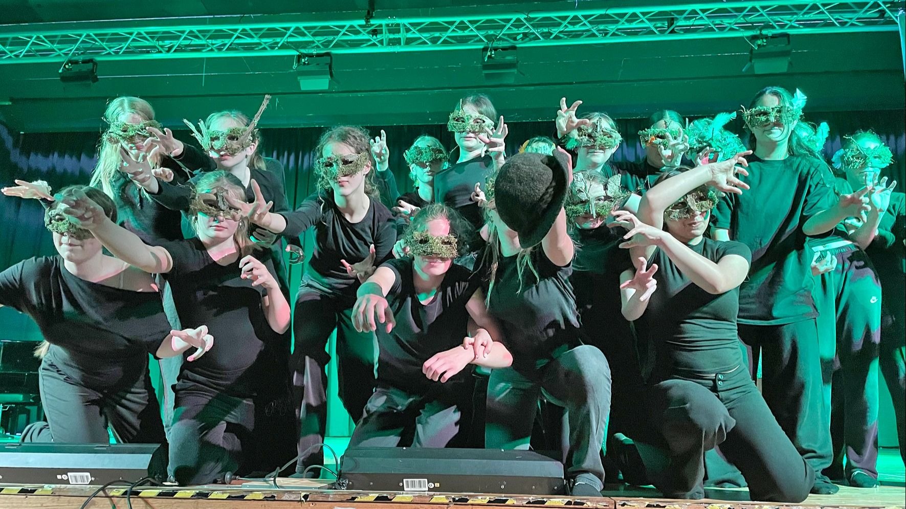 Eine Gruppe Asper Schüler mit grünen Blattmasken und schwarzen Kostümen posiert mit ausgestreckten Armen auf einer Bühne