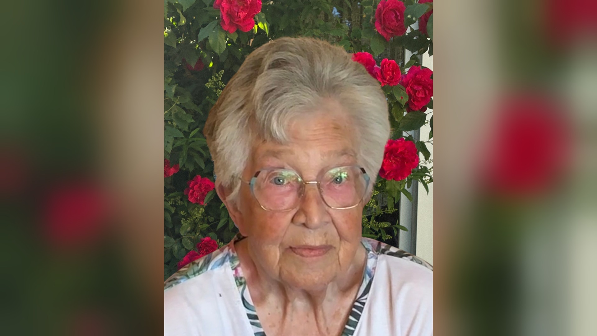 Renate Fischer, ältere Frau mit grauen Haaren und Brille, vor leuchtend roten Rosen und grünem Laub