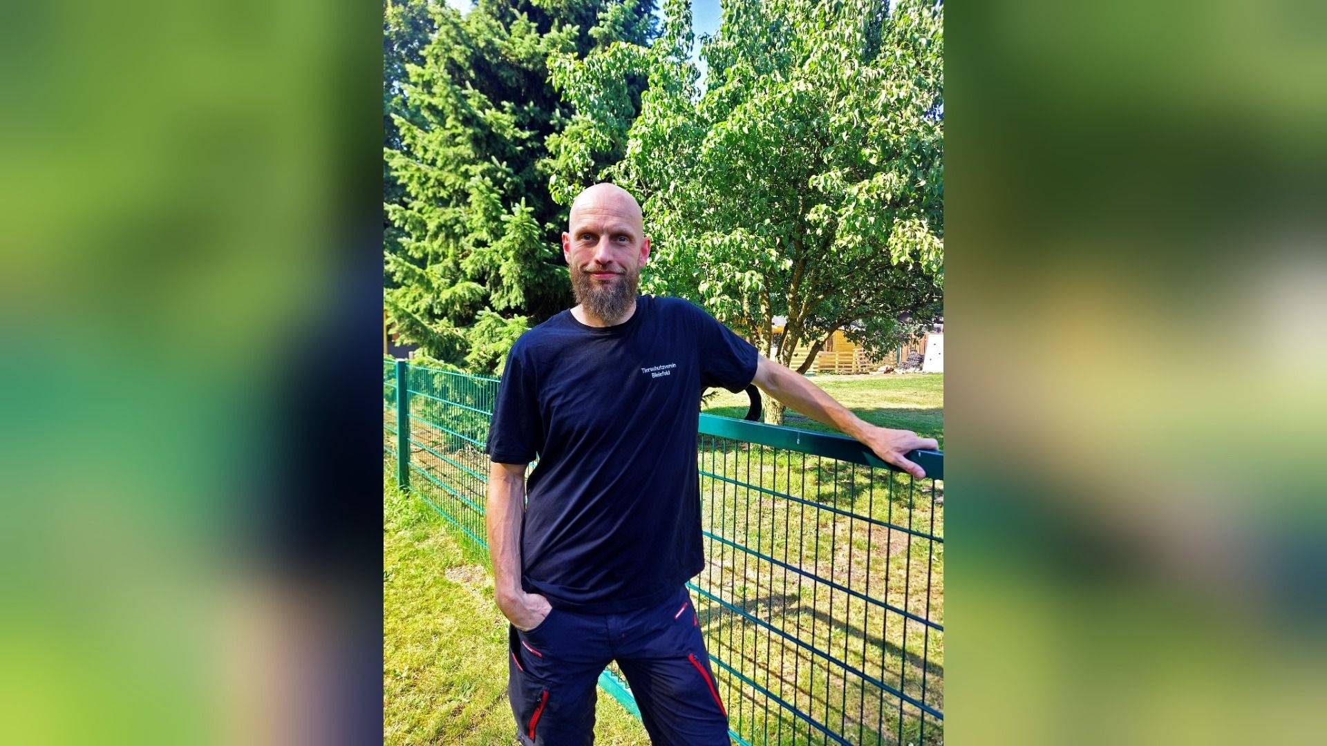 Jan Duhme, ein bärtiger Mann im T-Shirt des Tierschutzvereins Biesfeld, lehnt an einem grünen Zaun im Freien