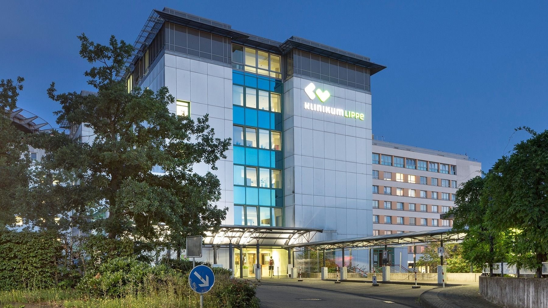 Beleuchtetes Gebäude des Klinikum Lippe am Abend mit Eingangsbereich, Bäumen und einer Zufahrtsstraße
