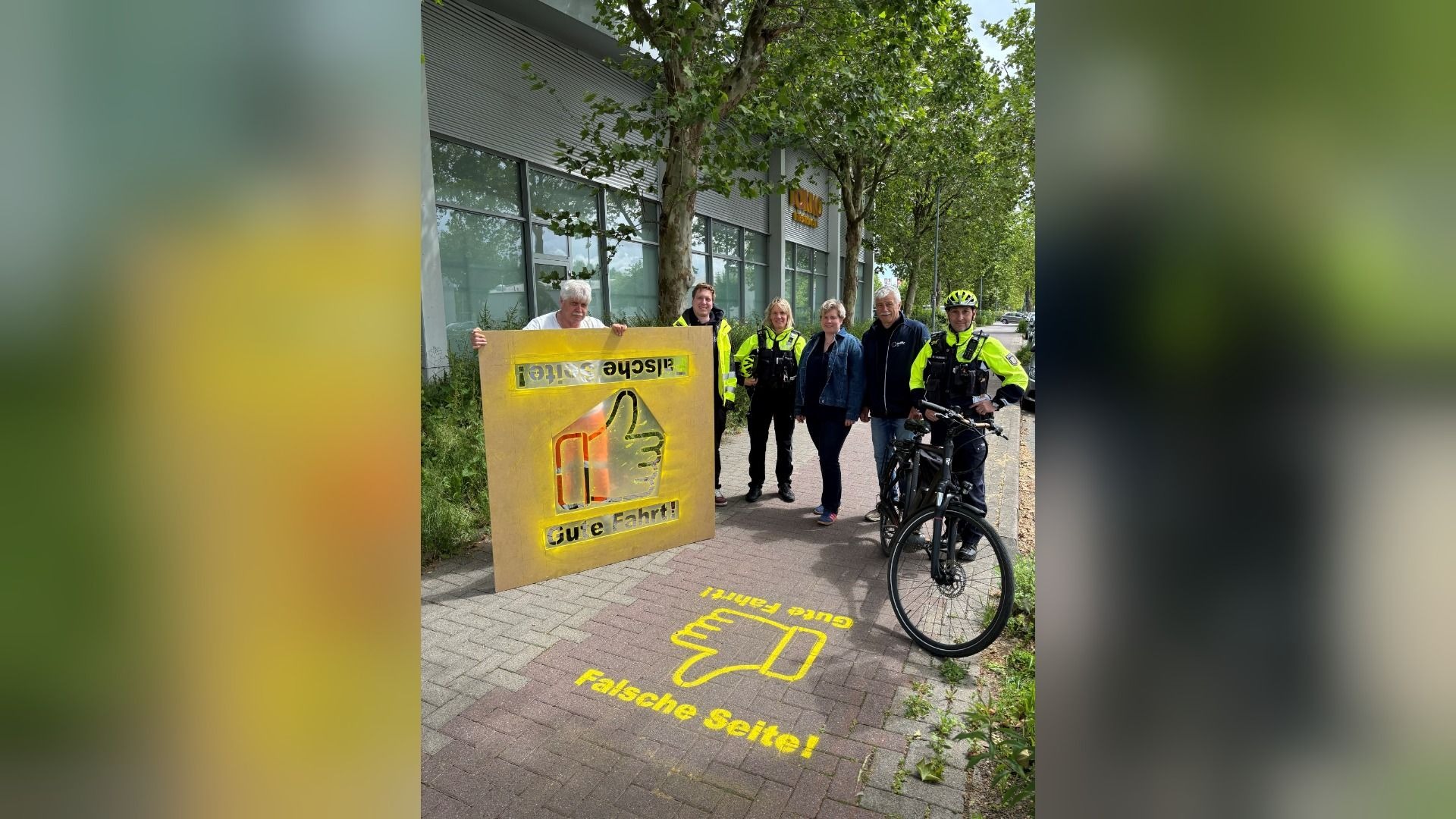 Zwei Polizisten, ein Radfahrer und drei weitere Personen mit Schildern zur sicheren Fahrtrichtung auf einem Weg