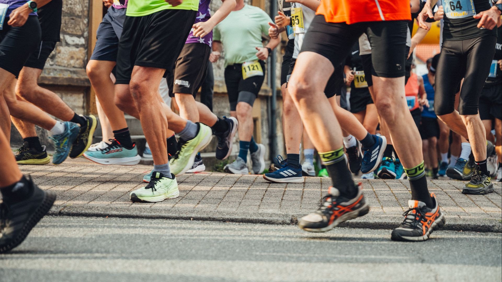 Viele Läuferbeine und bunte Sportschuhe in Bewegung auf einer Straße während eines Gemeinschaftslaufs