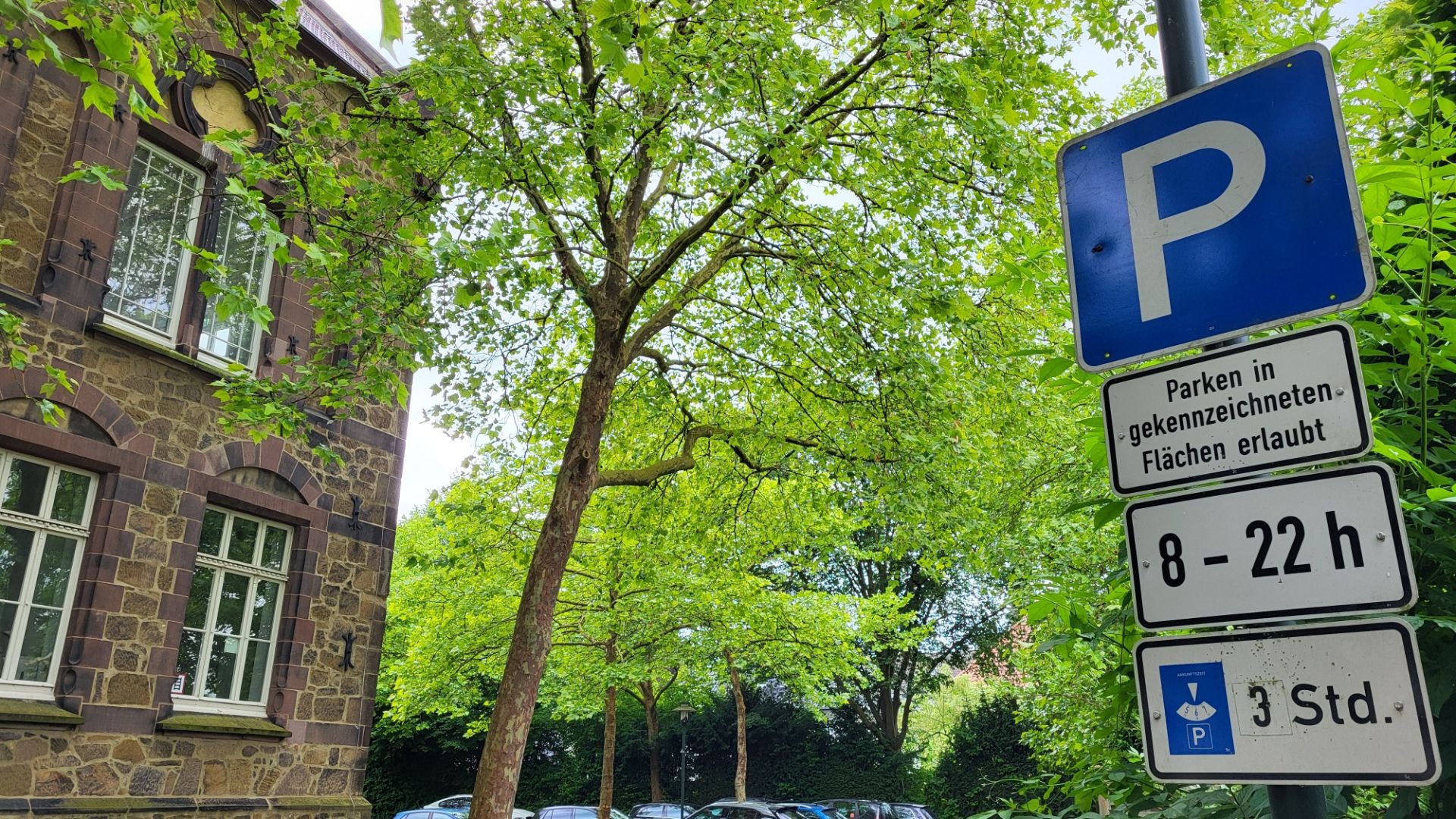 Blaues Parkschild mit drei Zusatzschildern: Parken von 8 bis 22 Uhr für maximal 3 Stunden, vor einem alten Steinhaus