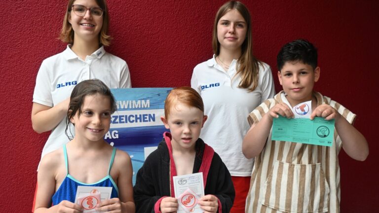 Zwei DLRG-Betreuerinnen und drei Kinder präsentieren stolz ihre Schwimmabzeichen und Urkunden vom Schwimmabzeichentag