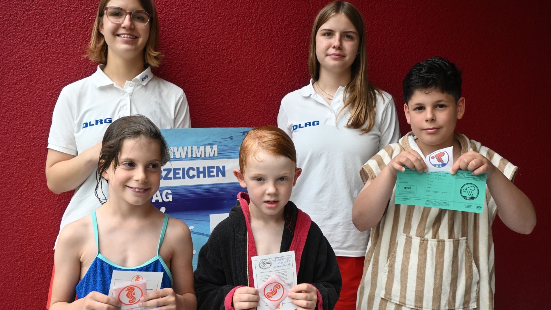 Zwei DLRG-Betreuerinnen und drei Kinder präsentieren stolz ihre Schwimmabzeichen und Urkunden vom Schwimmabzeichentag