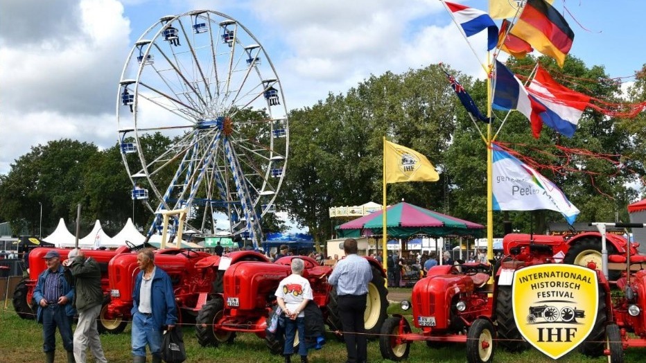 Rote Oldtimer-Traktoren und Besucher auf dem Internationalen Historischen Festival mit Riesenrad und wehenden Flaggen