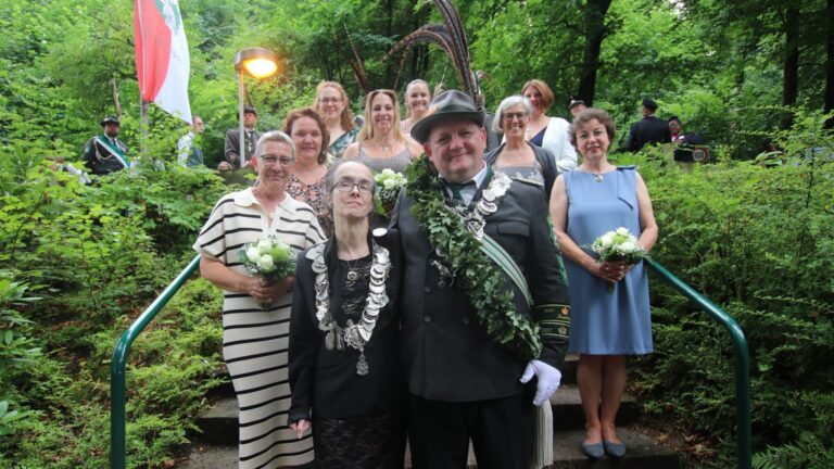 Eine Gruppe von Männern und Frauen in festlicher Kleidung, darunter ein Schützenkönigspaar mit Orden und Eichenlaub,