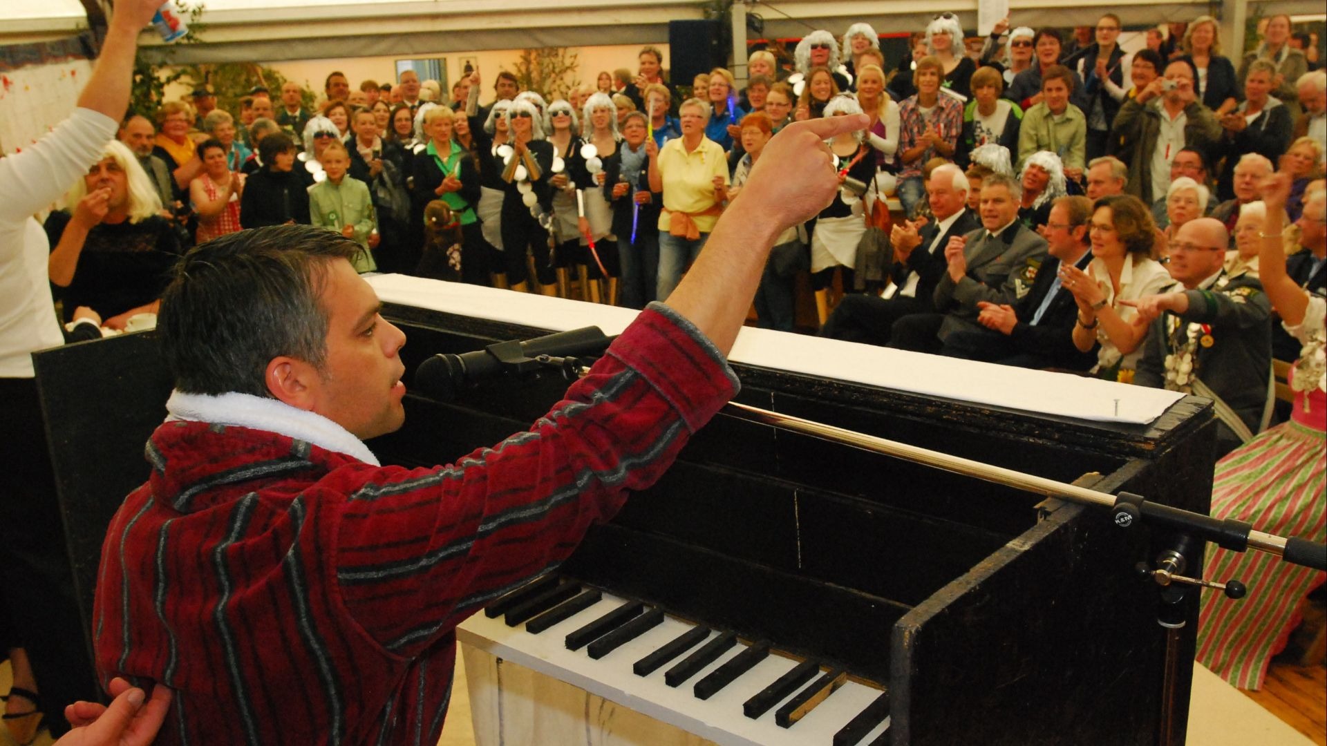 Mann in roter Streifenrobe performt am Klavier und zeigt auf eine begeisterte Zuschauermenge