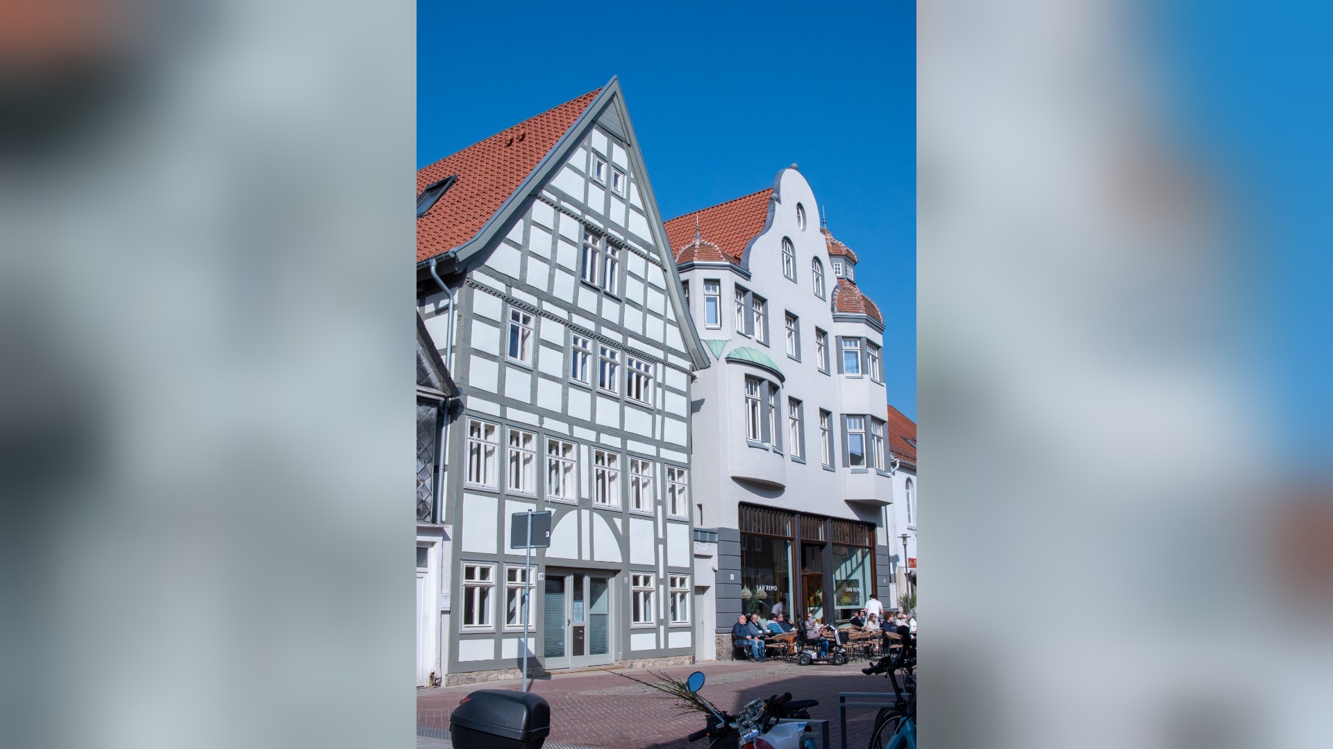 Zwei historische Gebäude mit roten Dächern in Lemgo, links ein Fachwerkhaus, rechts ein Eckhaus mit Erker und Außencafé