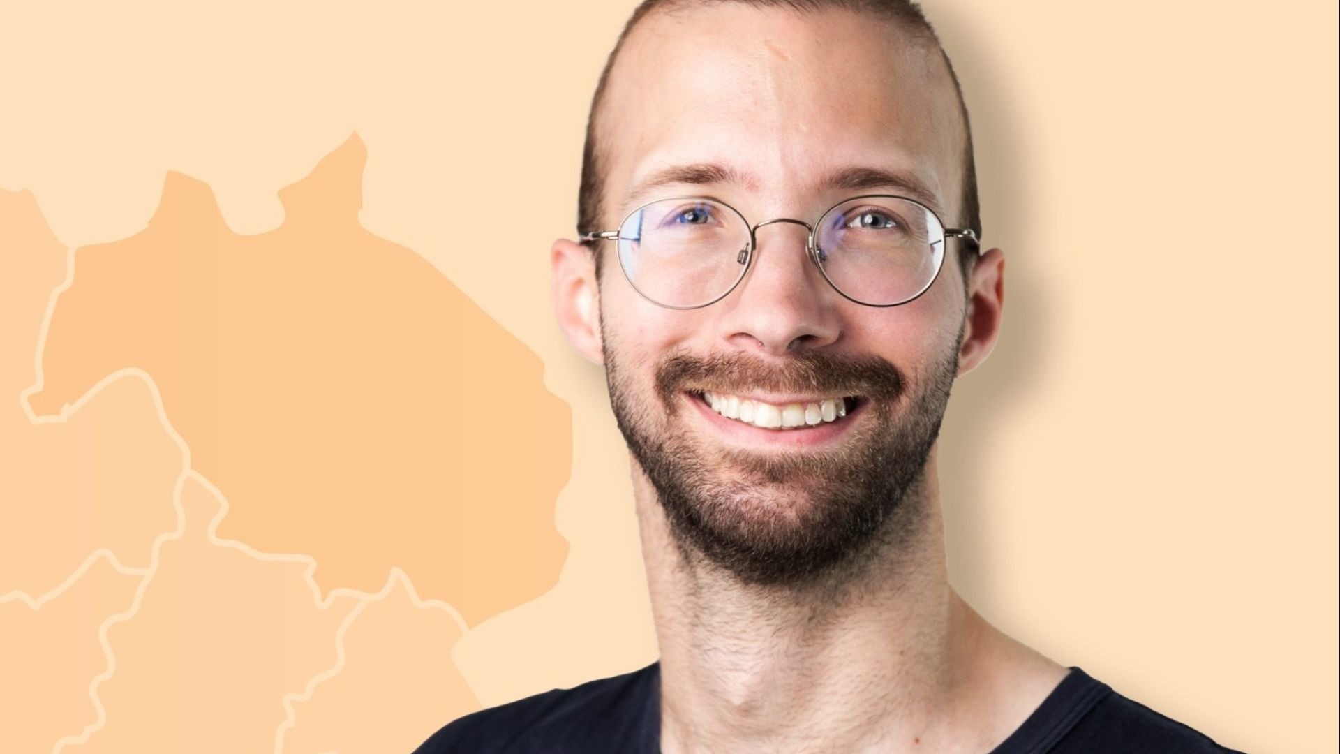 Julian Tienes, ein lächelnder Mann mit Bart und runder Brille vor einem hellorangen Hintergrund mit Landkartenumrissen